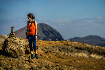 Young and attractive girl in orange shirt and blue leggings is hiking by the tourist's trail on Madeira island, Portugal. Sunny day.