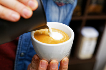 Closeup cup of cappuccino. Barista holding and pouring milk to make latte art.