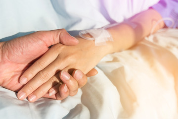 Close up. Hand of man hold hands with woman to encourage the patient saline solution in blue clothes lying on the hospital bed. Provide vascular nutrients.