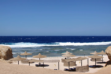 Tourists back to egypt resorts. Red sea beach with umbrella. Blue sky and big waves