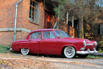 Old retro red classic car parked near old red brick house