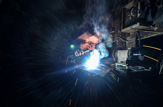 Operator, welder or worker welding some metal with welding machine behind the welding mask in the factory. Industrial concept image.