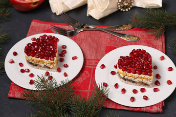 Festive salad in layers in the shape of a heart, decorated with pomegranate seeds on a dark background