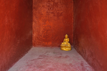 Small Buddha statue in front of red wall