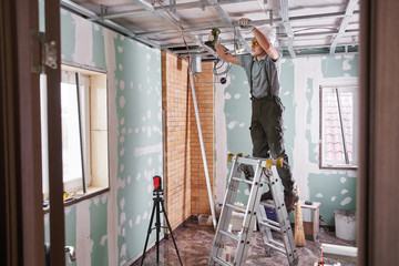 Room repair. Interior finish. young builder makes a plasterboard ceiling, standing on a stepladder