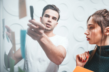 Coworking people discussing new business plan and posted on a sticky glass note wall. Intelligent...