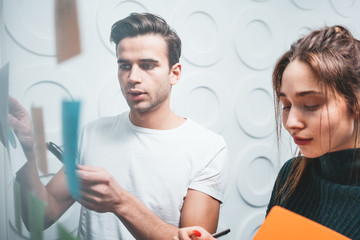 Obraz premium Business partners discussing together about new pnal in big open space office. Two coworkers standing behinde glass stiky wall and brainstorming new startup ideas