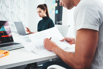 Obraz premium Two young coworker working toogether at work place office while sitting at the table. Team of business people analyze document and blueprint plan