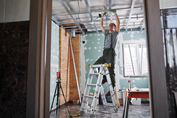 Fototapeta premium Room repair. Interior finish. young builder makes a plasterboard ceiling, standing on a stepladder