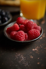 Close up on fresh raspberries placed on ceramic saucer on dark rusty table. Selective focus. Healthy breakfast ingredient.