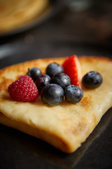Close up on pancake with fresh fruit topping placed on dark rusty table. Selective focus. Healthy homemade breakfast concept.
