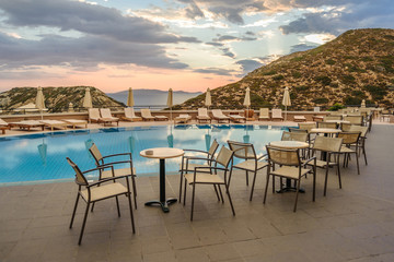 Fototapeta premium Tables and chairs near the pool against the background of the morning sky and the sea