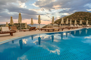 Sun beds and umbrellas near the pool against the background of the morning sky and the sea. .