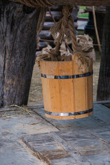Close up of wooden bucket hanging from log over groundwater well
