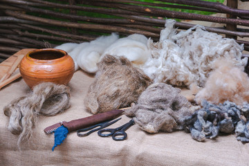 Traditional earthenware crockery pot, packs of sheep wool, hand shears, scissors and other tools on linen covered table. Medieval reconstruction