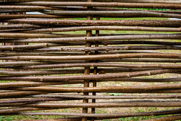 Textured background of handmade wattle fence and green grass behind it