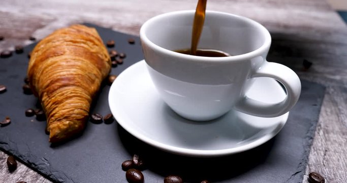 Pouring a cup of coffee to serve with a tasty croissant. Coffee beans all arround. Beautiful composition.
