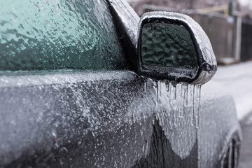 Frozen mirror of a car with iciclas on it in winter timea