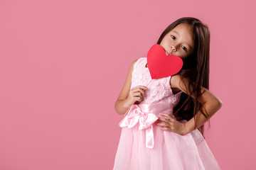 portrait of a cute little girl in a pink dress holding a paper heart on a pink background. St. Valentine's Day