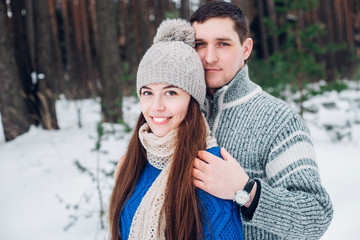 Fototapeta premium Embracing couple hugging and looking at camera with smiles in winter park