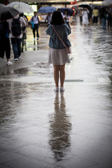 Lone girl and reflection standing in rain with umbrella in a busy street