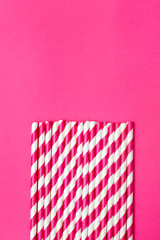 Bright pink paper straws on a bright pink background. Vertical
