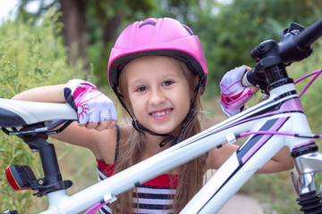Naklejka premium Little cute girl in a pink helmet near a bicycle