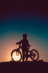 Plakat Silhouette of a little girl with a bicycle at sunset
