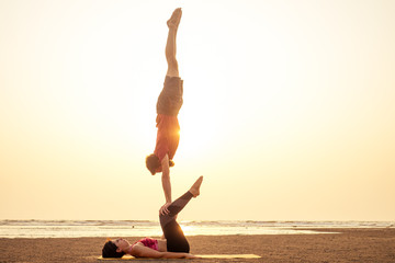 Fototapeta na wymiar two young man and beautiful woman on beach doing fitness yoga exercise together. Acroyoga element for strength and balance at sea octan goa india sunset