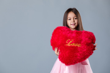 portrait of a cute little girl in pink dress hugging big red heart on gray background. St. Valentine's Day