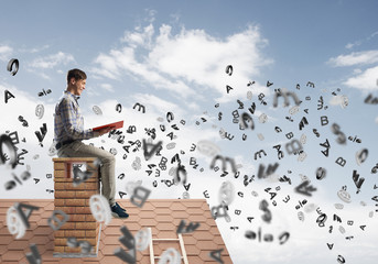 Man on brick roof reading book and symbols flying around