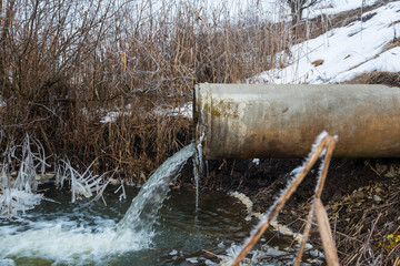 Fototapeta na wymiar Concrete pipe transporting the polluted water to a small pond at wintertime.