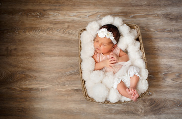 Newborn girl with a lion toy in her arms sleeps in the basket covered with white fur blanket on the floor; brown background