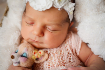 Newborn girl with a lion toy in her arms sleeps in the basket covered with white fur blanket on the floor