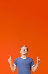 Cute little boy pointing up on orange background