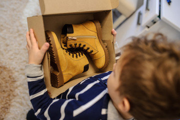 topview of a boy holding a open cardboard box with a pair of yellow leatrher boots