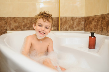 Little boy washing and playing in bathtub with foam and soap bubbles