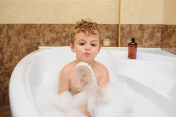 Little boy washing and playing in bathtub with foam and soap bubbles