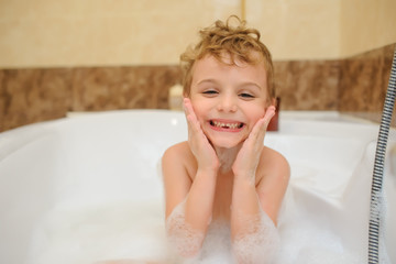 Naklejka premium Little boy washing and playing in bathtub with foam and soap bubbles