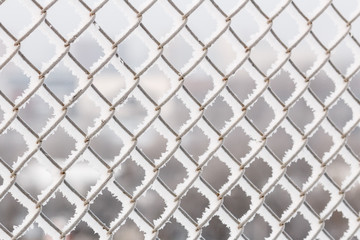 Abstract background of wire fence in winter, covered with frozen snow and ice. Shallow depth of field, blurred background