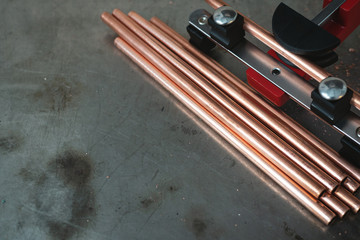 Pipe bender tool and a brass pipes on a workbench of fitter background with copy space.