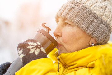 Adult woman in yellow winter jacket enjoying coffee on a winter day. 