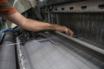 Hand on weaving machine. A loom machine for clothing or woven label. Weaving machine for garment industry. Weaving loom in textile factory. Industrial fabric production line in 