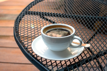 A cup of coffee on Black steel grating table in the morning.