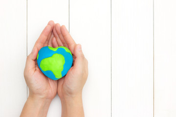 Hands holding global heart shape over white wooden background with copy space. Happy mother earth day concept. Top view. Flat lay. Minimal style.