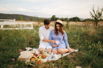 Future mom and dad sits in field. Pregnant woman with her husband put their hands on belly