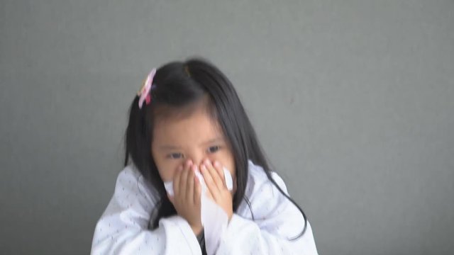 Asian child or kid girl sick with sneezing on nose and cold cough on tissue paper because weak or virus and bacteria from dust weather and kindergarten and pre school for medical background on slow