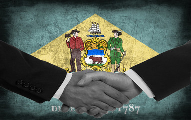 Two men/politicians in suits shaking hands with the national flag on the background - Delaware - United States