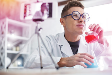 Chemistry student smelling test tube with colorful liquid sitting in laboratory