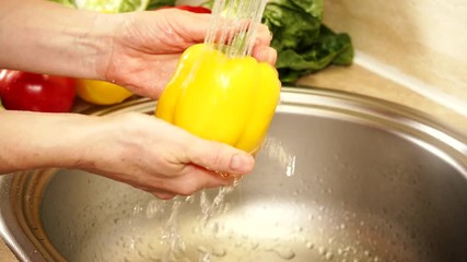 Female hand washing fresh yellow paprika vegetable in kitchen sink under water stream. Cleaning products. Ingredient for cooking or tasty salad. Healthy eating, dieting concept - Powered by Adobe